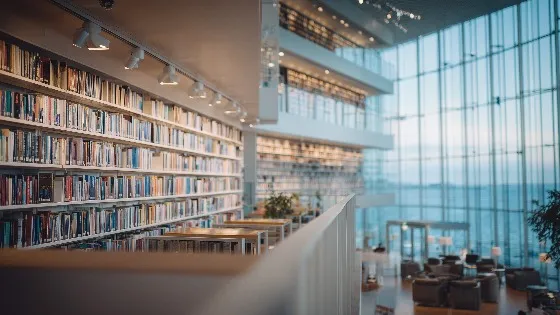a vast library of books on a wall-sized bookshelf in a large room with floor to ceiling windows