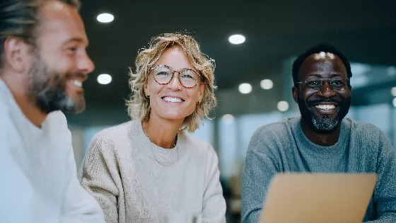 the middle-aged professionals collaborate at a table in an office. All are smiling.
